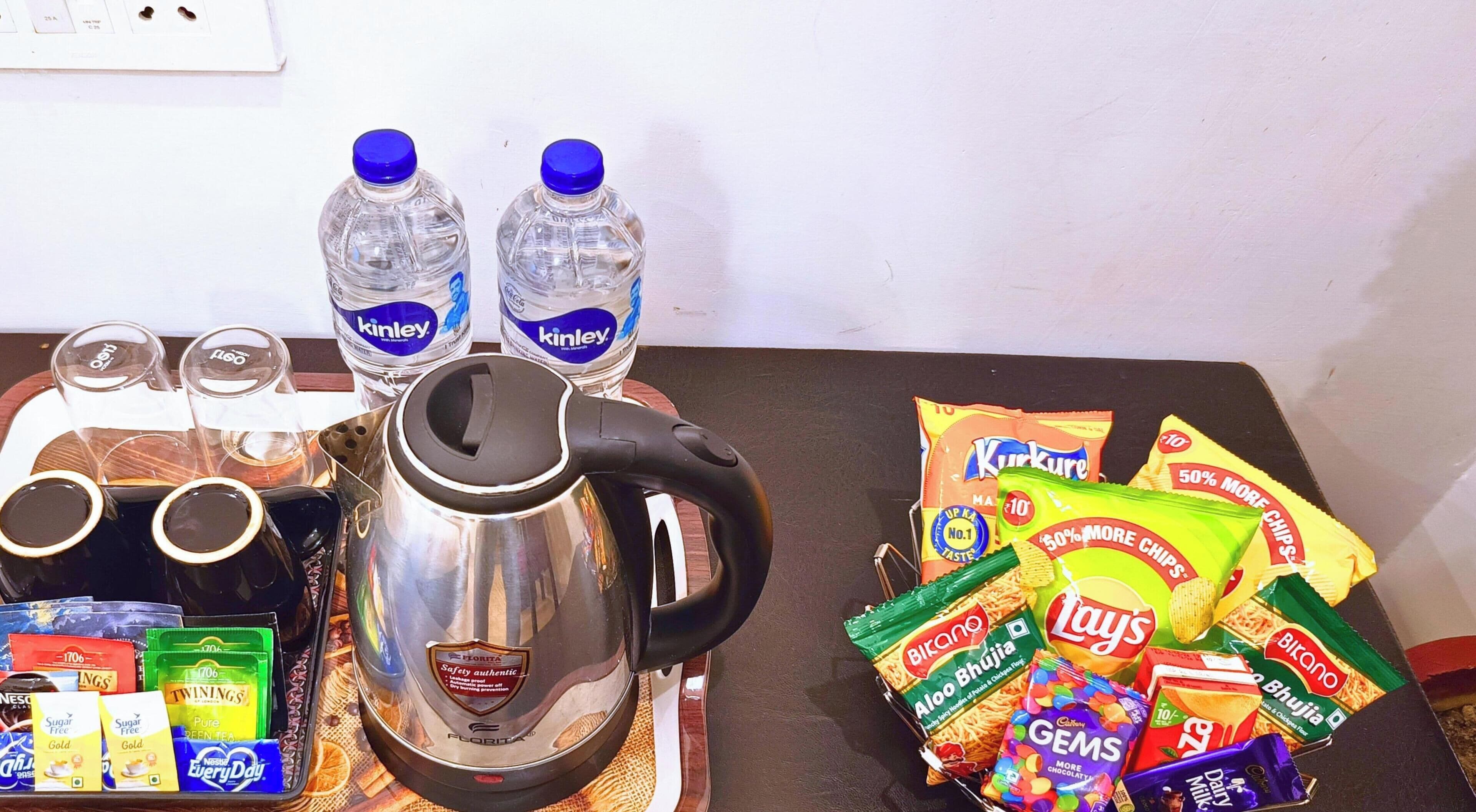 A table with a coffee maker, water bottles, glasses, and snacks including chips and chocolate.