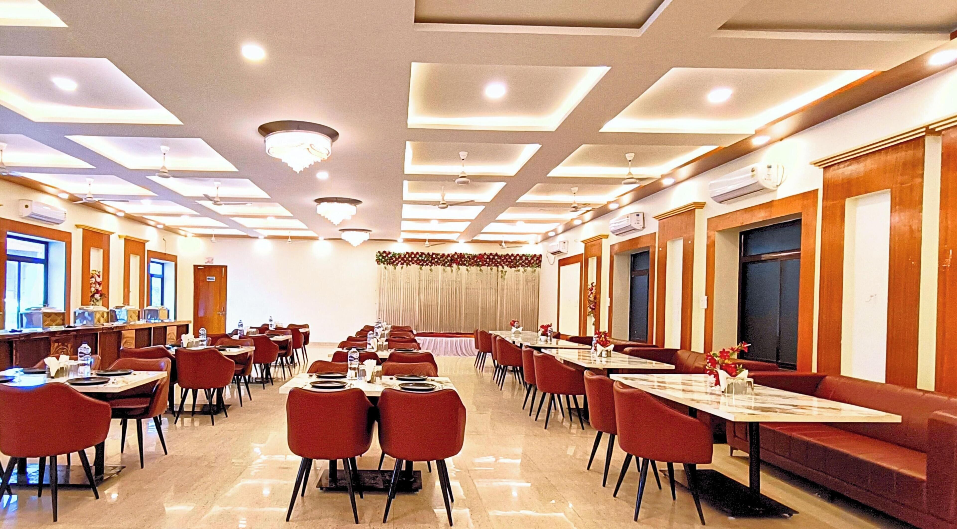 A hotel dining area with multiple tables and chairs, ceiling lights, and air conditioning units.