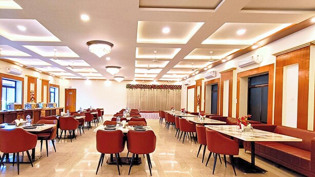A hotel dining area with multiple tables and chairs, ceiling lights, and air conditioning units. - Trayamb Inn by Asapian Hotels (Faizabad)