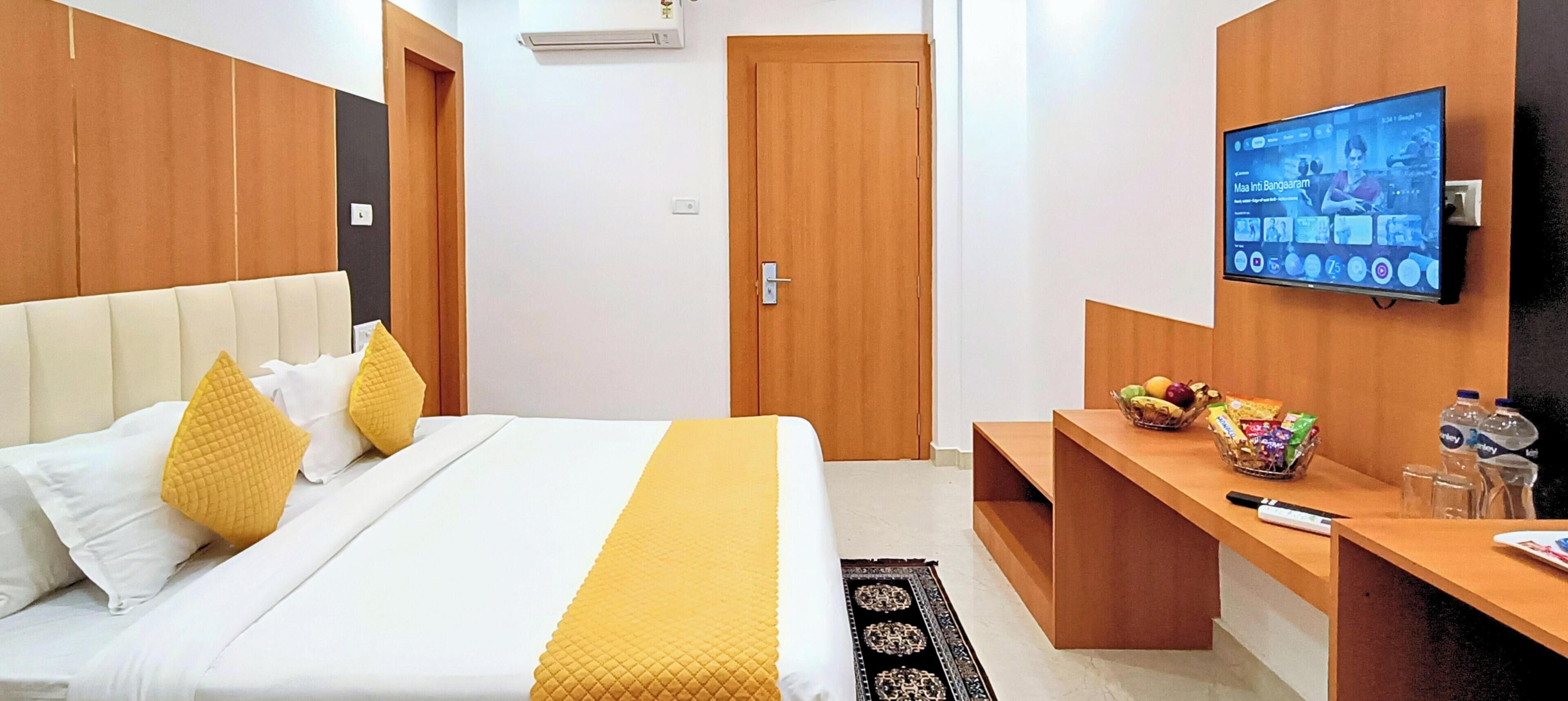 A hotel room with a bed, a TV, a desk with snacks, and a door.