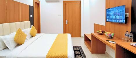 A hotel room with a bed, a TV, a desk with snacks, and a door.