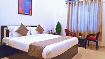 A hotel room with a bed, a nightstand, a chair, a small table, and a window with curtains.