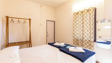 A hotel room with a bed, a wooden rack, a door, a patterned curtain, and a mirror reflecting a bed.