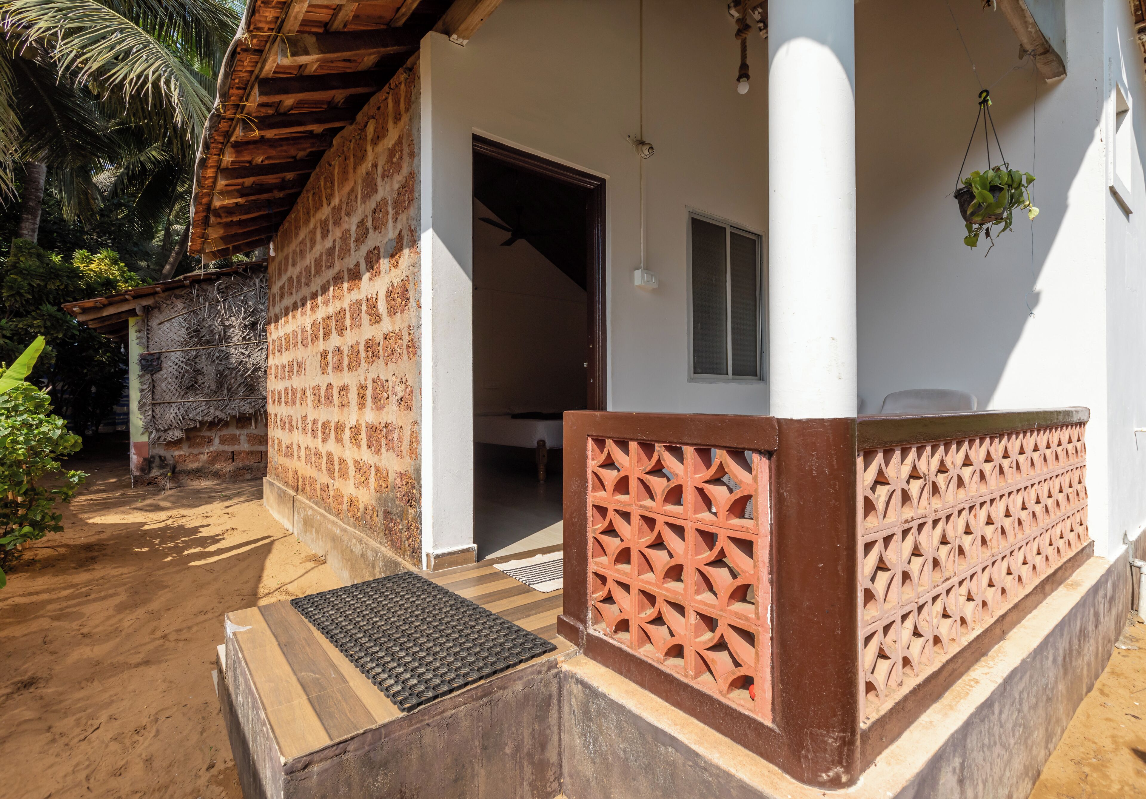 A covered outdoor area with a wooden bench, a door leading inside, and a hanging plant.