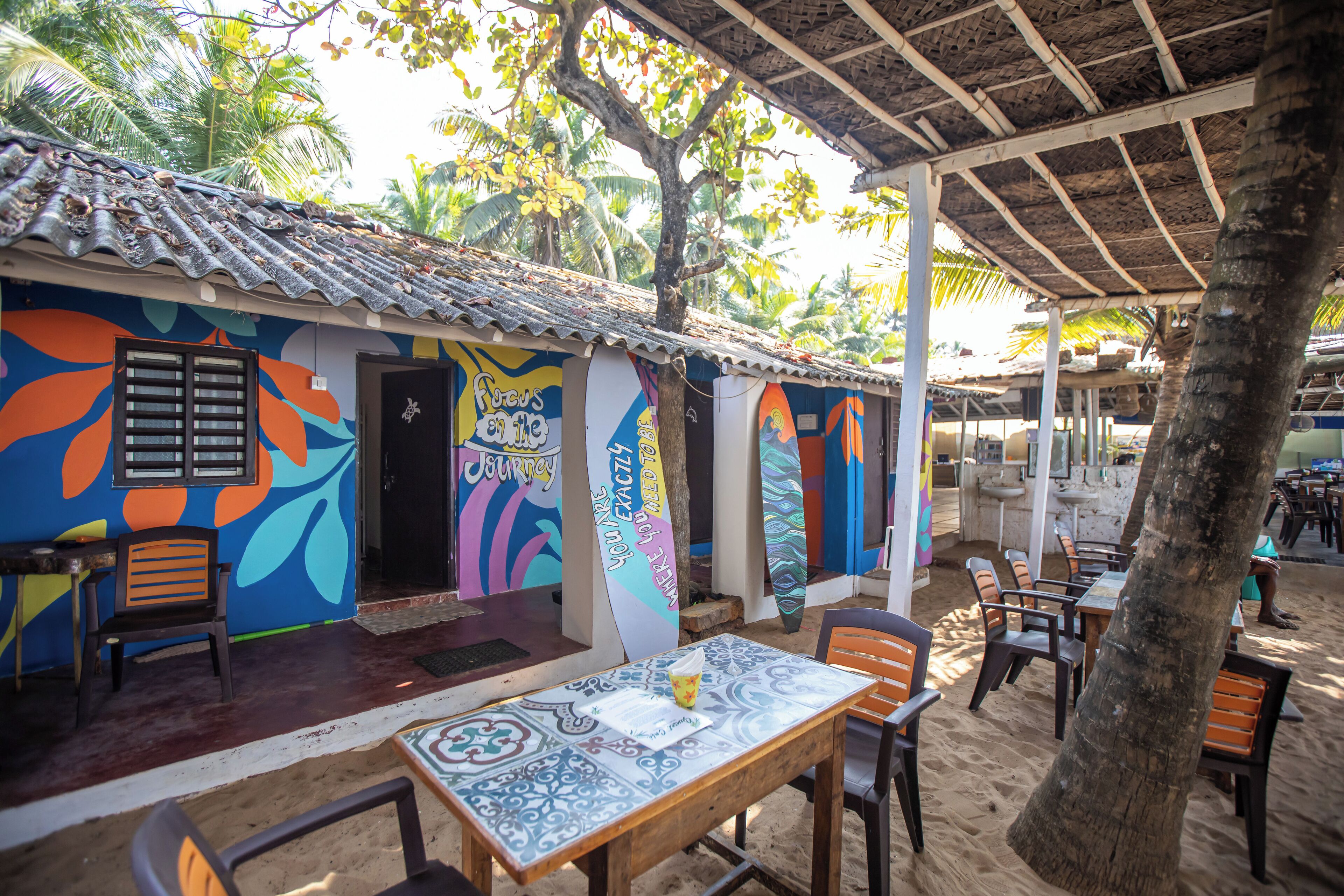 Um restaurante à beira-mar com murais coloridos, mesas ao ar livre e um telhado de palha.