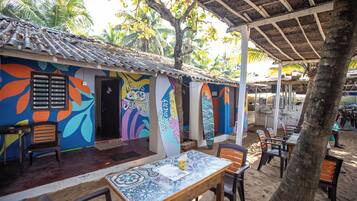 Um restaurante à beira-mar com murais coloridos, mesas ao ar livre e um telhado de palha.