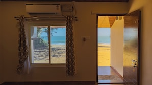 Una habitación con vistas a una playa a través de una ventana, una puerta con diseño geométrico y un equipo de aire acondicionado en la pared.