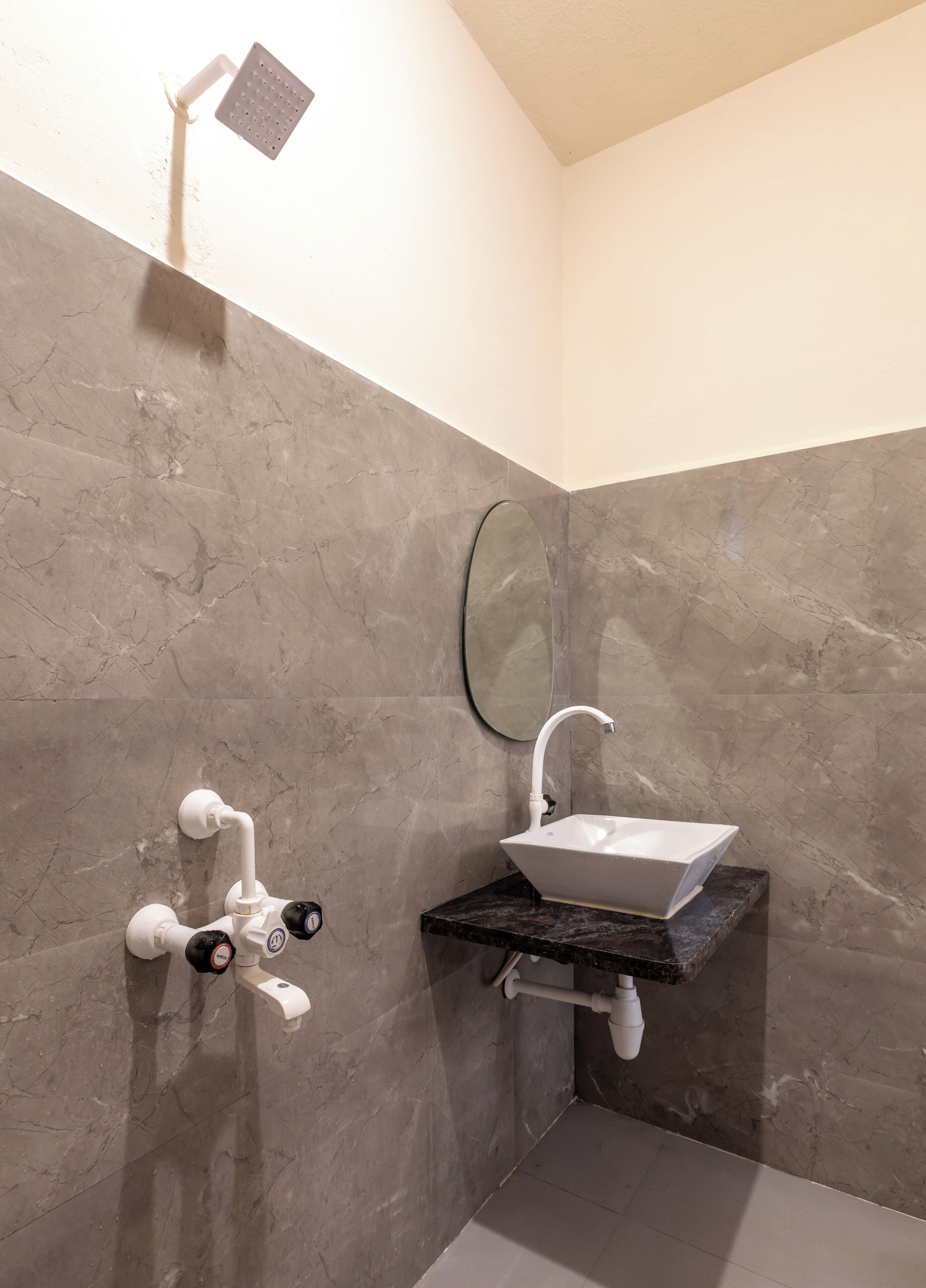 Een badkamer met een marmeren wand, een witte wastafel en een douchekop.