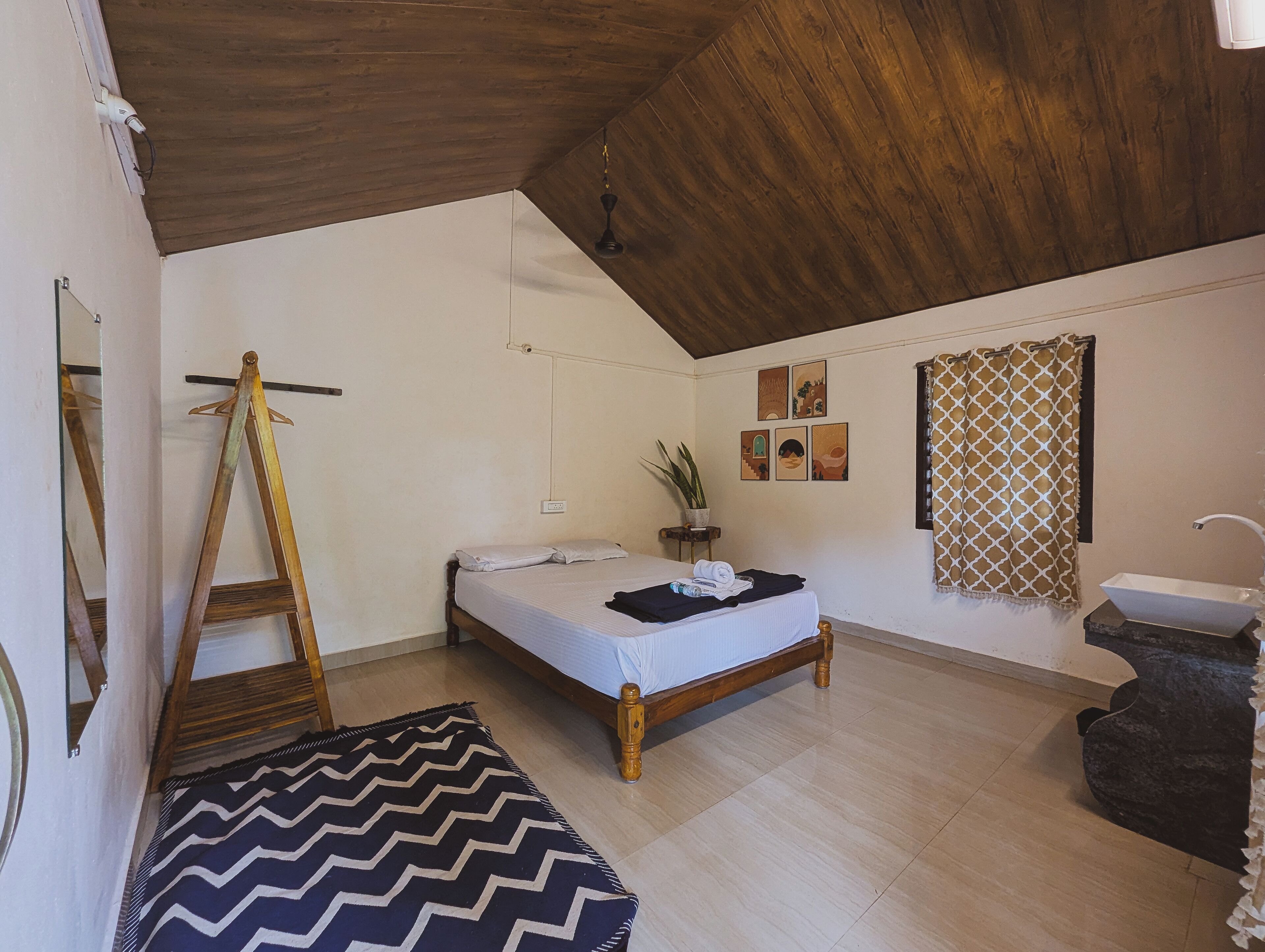 A bedroom with a wooden bed, a desk, a chair, a potted plant, and a bathroom with a sink and shower.