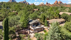 A modern house with a balcony, surrounded by dense greenery and red rock formations in the background. - The Sedona Sanctuary: Hot Tub & Unbeatable Views (Sedona)
