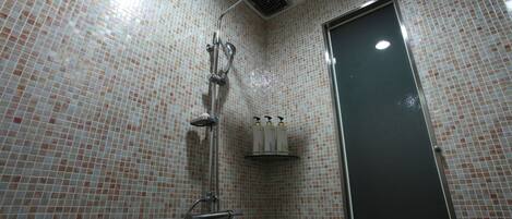 A bathroom with a tiled shower area, a door, and a shelf with toiletries.