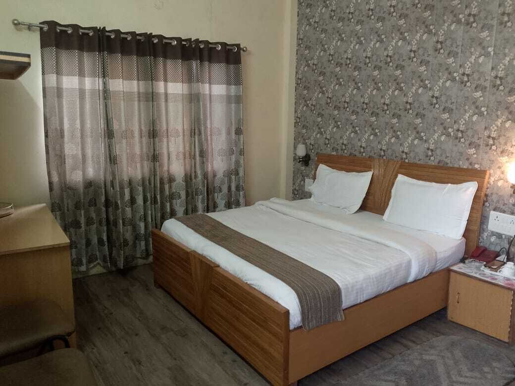 A bedroom with a wooden bed, a nightstand, a desk, and a patterned wallpaper.