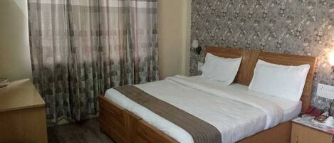 A bedroom with a wooden bed, a nightstand, a desk, and a patterned wallpaper.