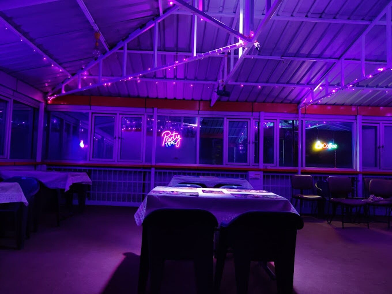 An indoor dining area with tables and chairs, a neon sign reading "Party Time," and a window with a sign that says "Coffee."