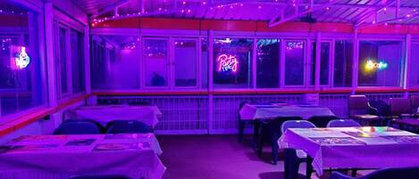 Un espacio interior para comer con mesas y sillas, un letrero de neón y una ventana con vistas.