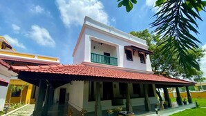 A two-story building with a red-tiled roof, a balcony with green railings, and a covered entrance area with potted plants. - FRANCO TAMIL VILLAS (Puducherry)