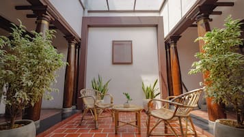 Een terras met rieten meubels, potplanten en een lijst met foto aan de muur.