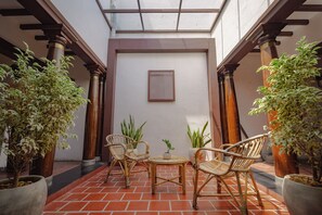 A patio area with wicker furniture, potted plants, and a framed picture on the wall. - FRANCO TAMIL VILLAS (Puducherry)