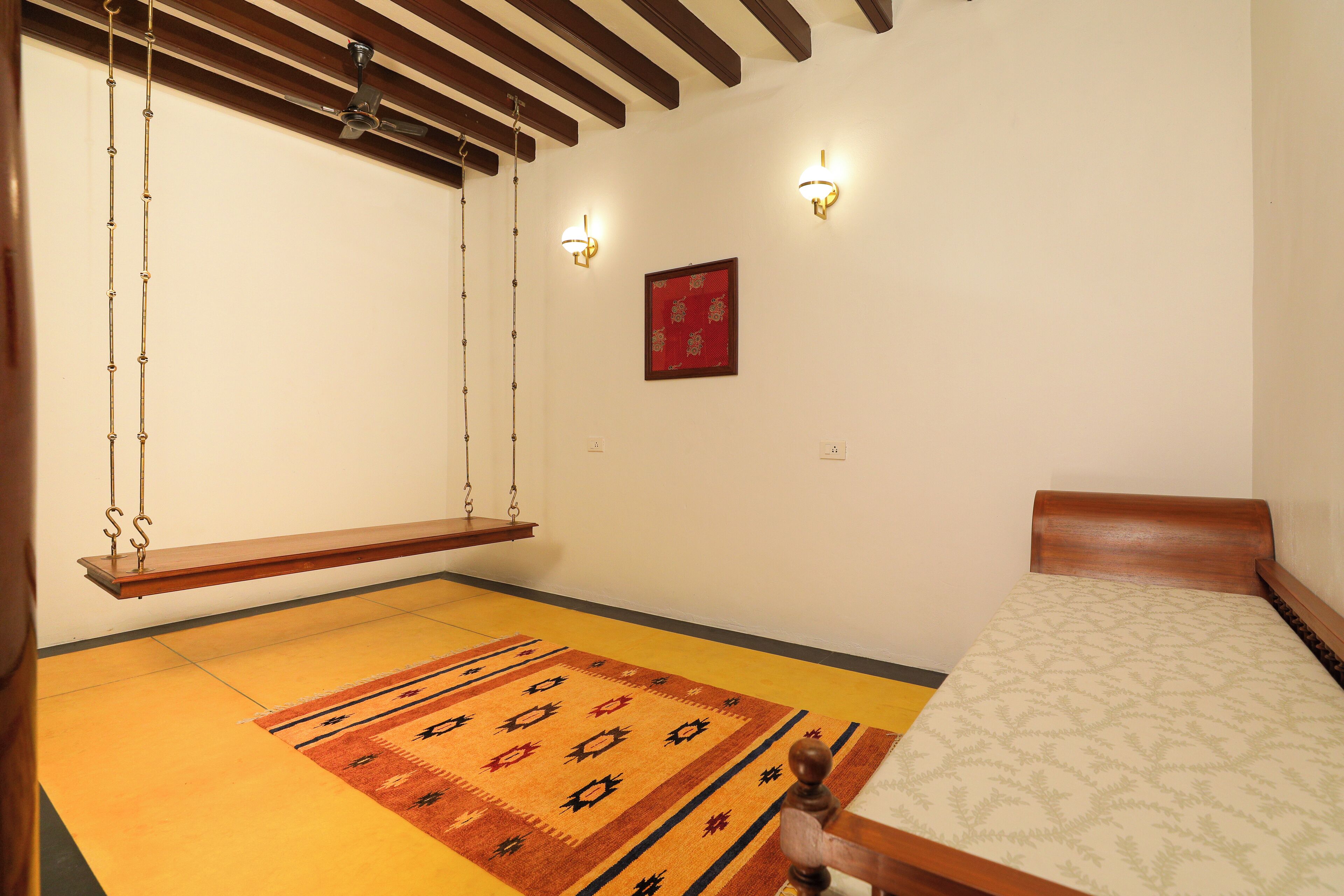 A room with a bed, a hanging swing, a patterned rug, and a red decorative piece on the wall.