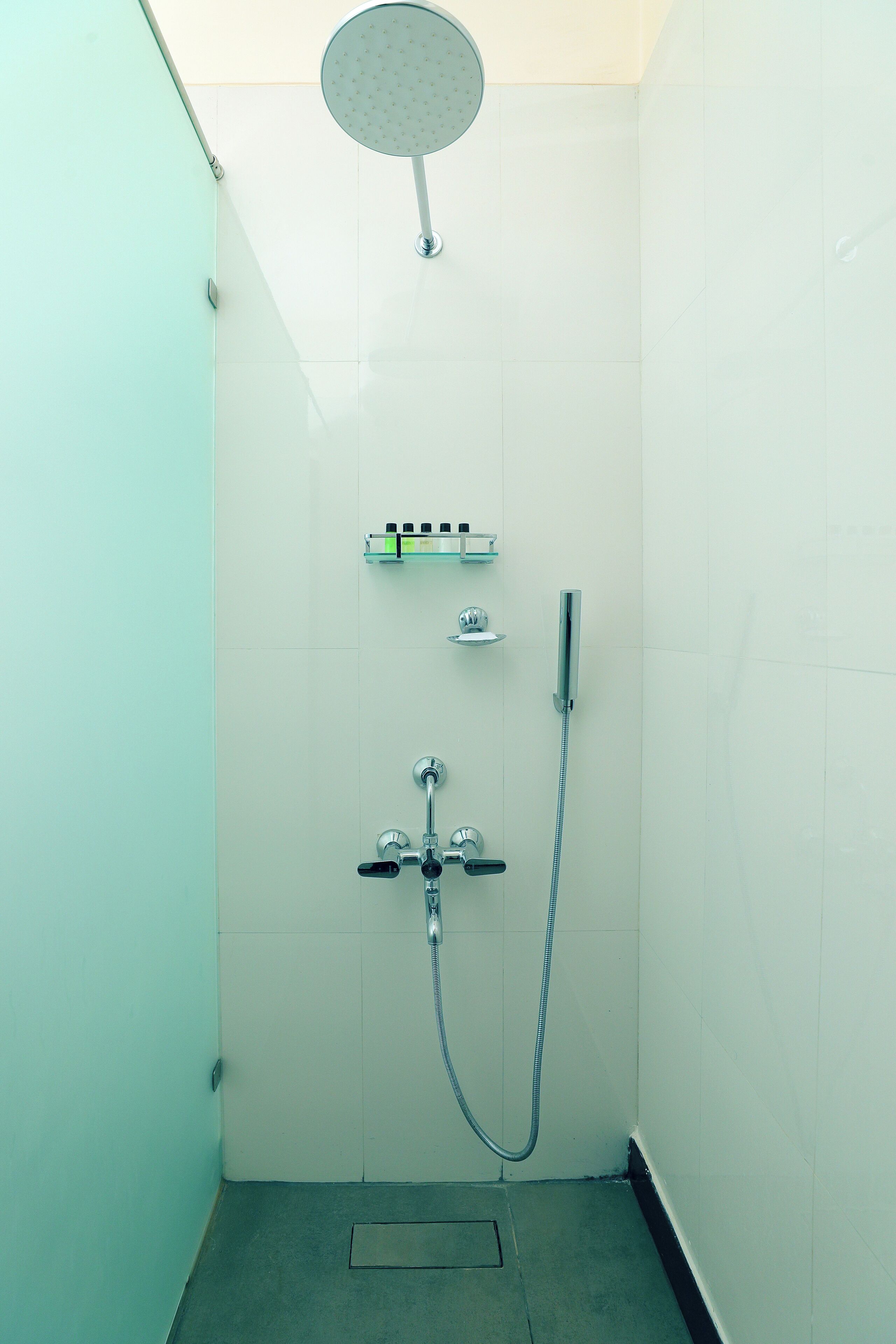 A small, tiled shower room with a handheld showerhead, a wall-mounted faucet, and a soap dish.