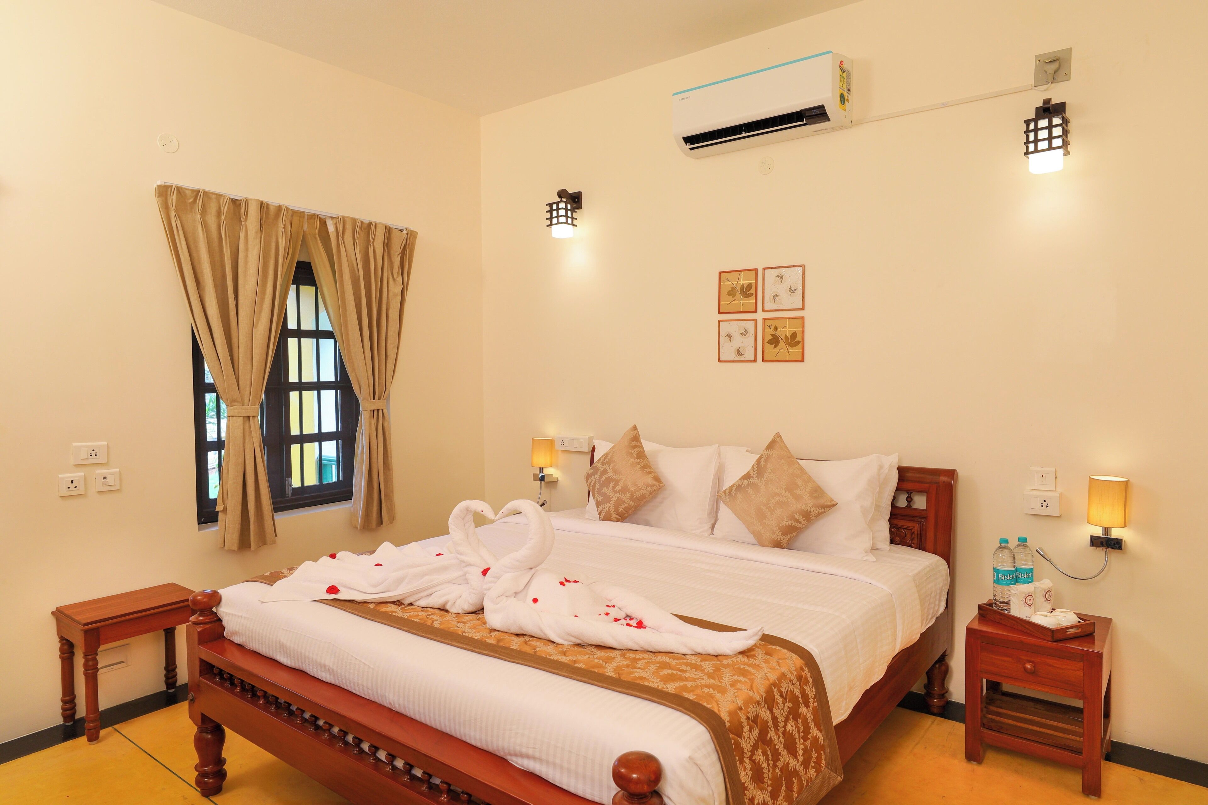 Habitación de hotel con cama, mesitas de noche, unidad de aire acondicionado, luces fijadas en la pared y ventana con cortinas.