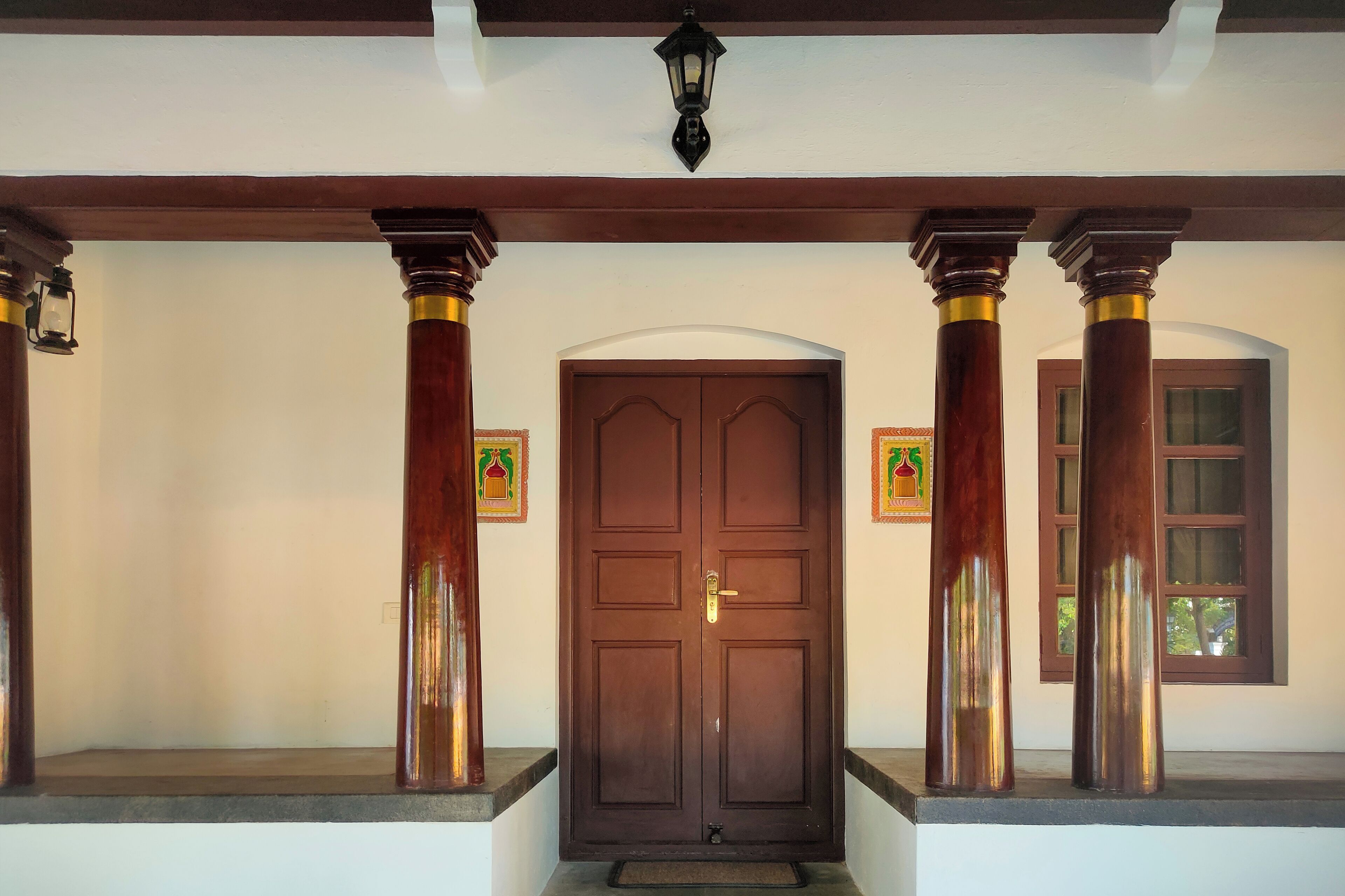 A wooden door with a brass handle, flanked by two columns with gold accents, and a small window to the right.