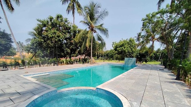 A swimming pool with a tiled edge, surrounded by a paved walkway and palm trees. - FRANCO TAMIL VILLAS (Puducherry)