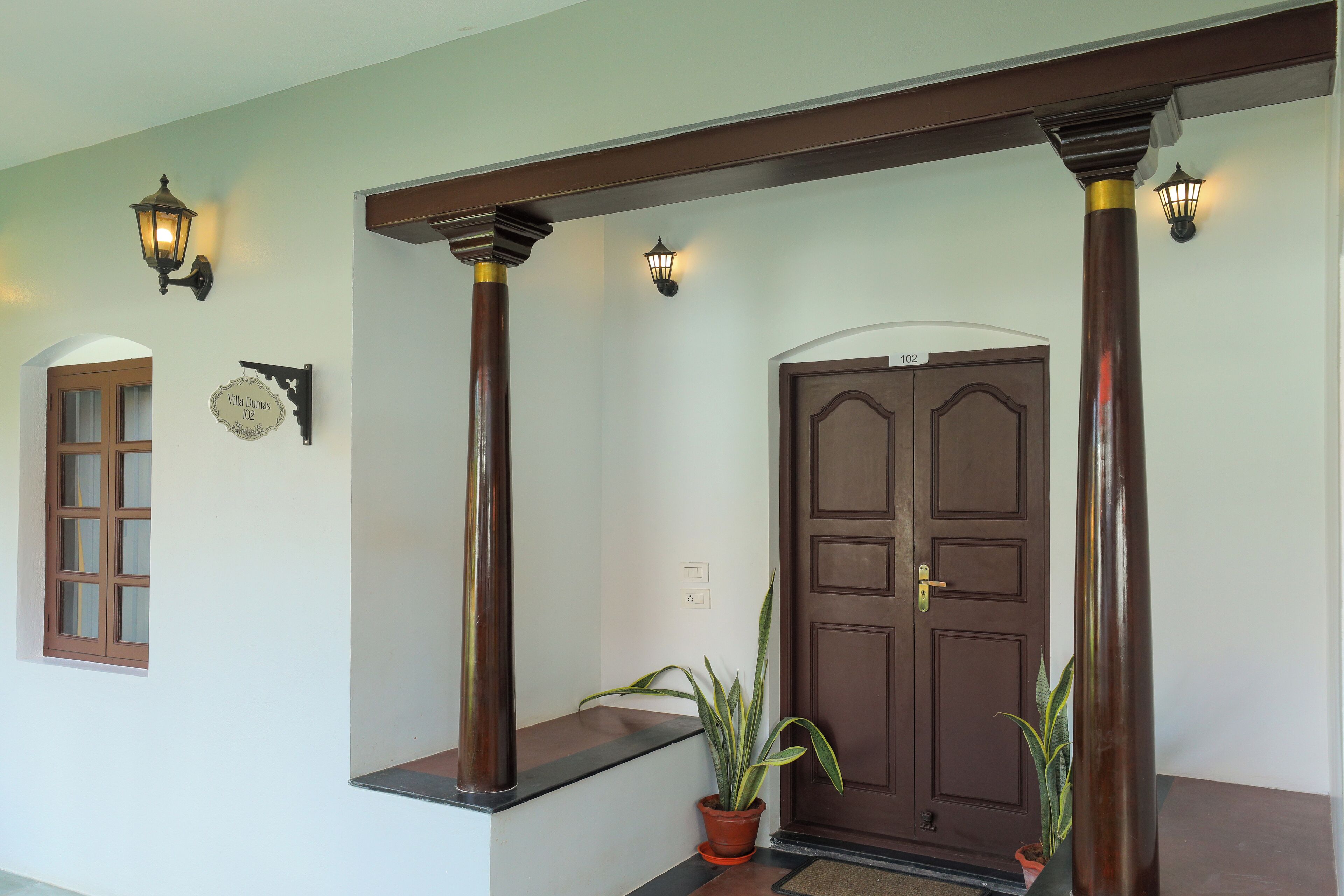 A wooden door with a number plate, a potted plant, and a bench.