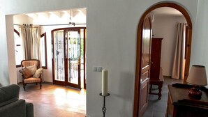 A spacious living area with a wooden chair, a lamp, and a view through a glass door to an outdoor patio. - Beautiful and comfortable villa in Calpe, Costa Blanca, Spain  with private pool for 4 persons (Calpe)