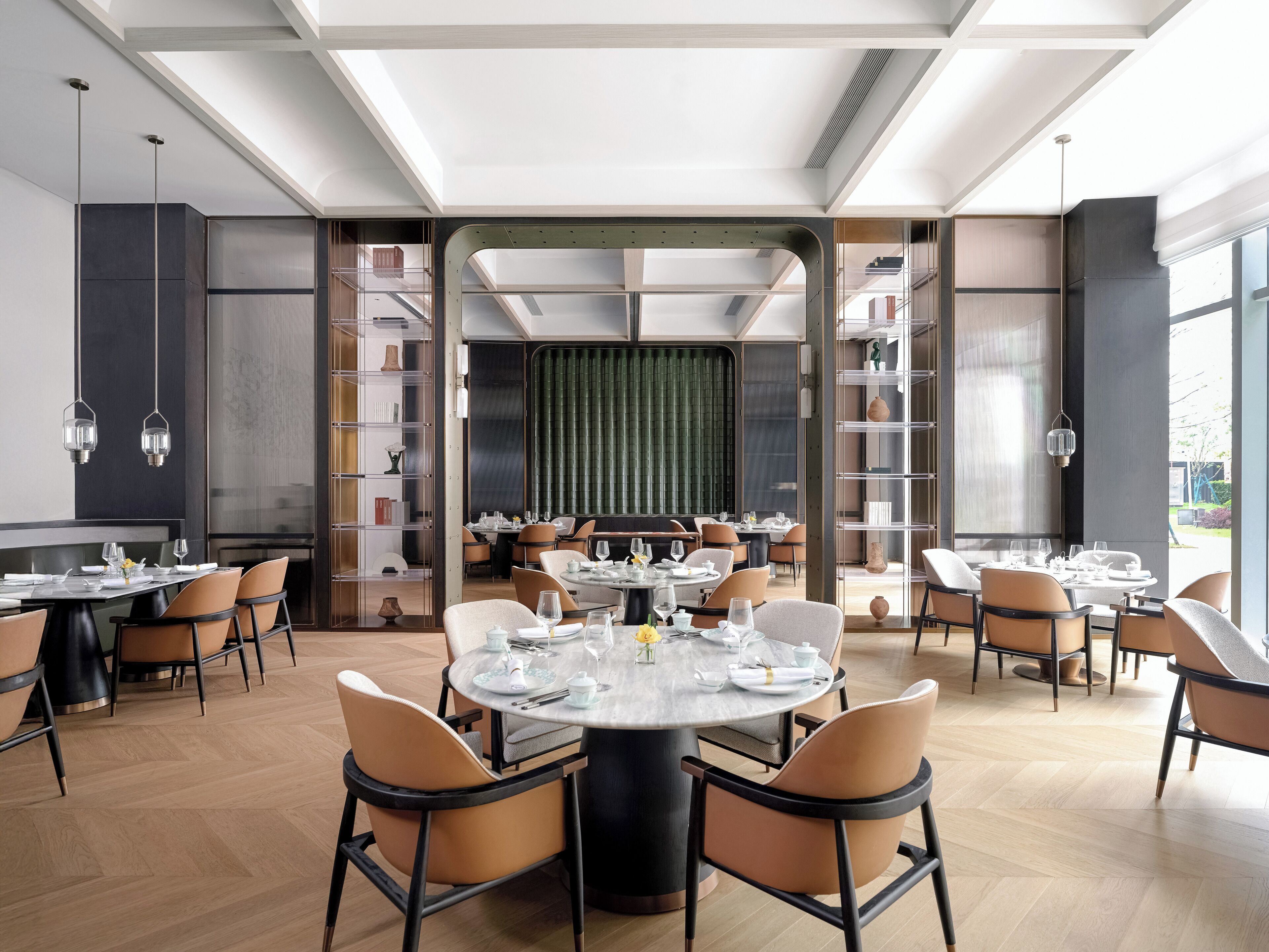 Een ruime eetruimte met ronde tafels, moderne stoelen en een centraal glazen scheidingswand.