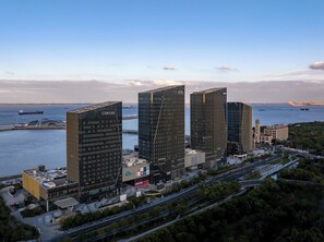 A modern building complex with three tall skyscrapers, a waterfront, and a busy road with greenery. - Cordis Shanghai Seaworld (Shanghai)