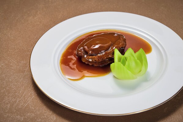 Un plato con un guiso de carne y salsa, y una guarnición verde sobre un plato blanco.