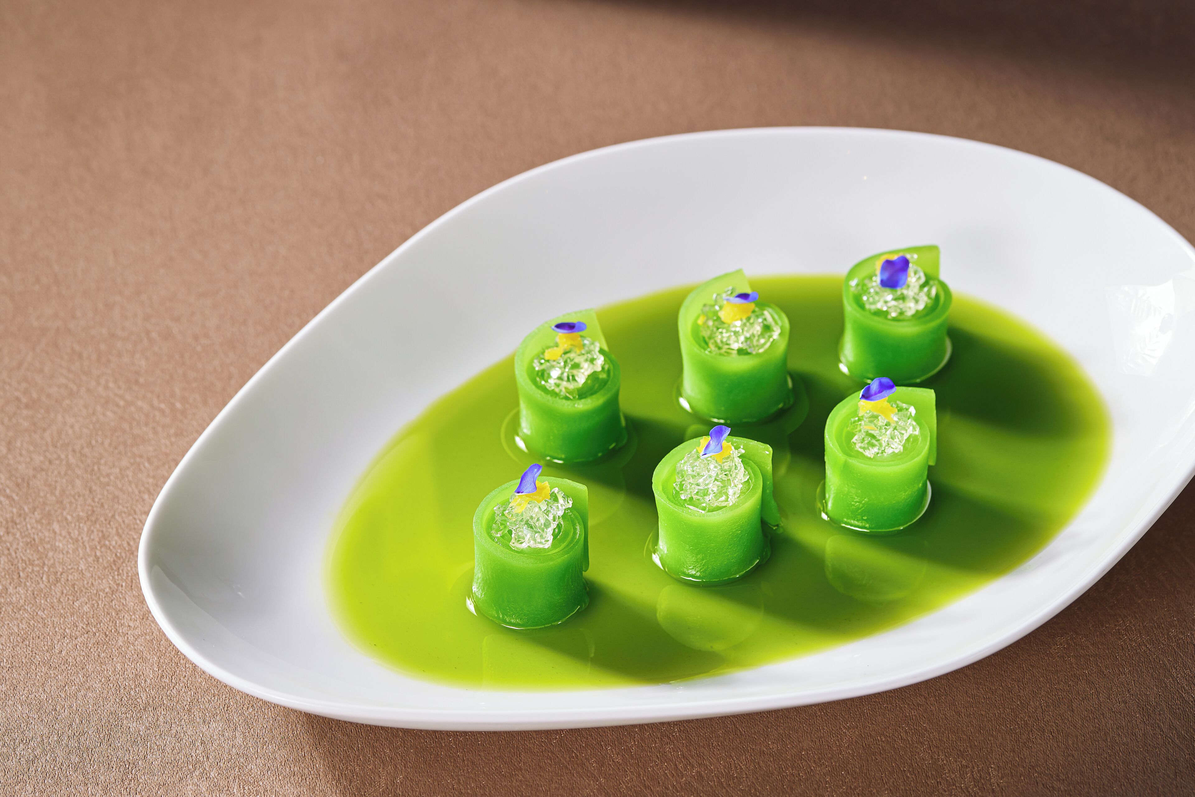 A white plate with six green cylindrical desserts on a brown surface.