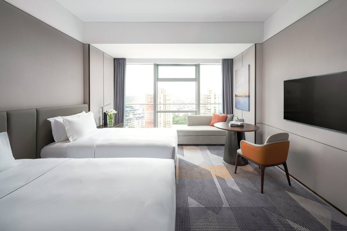 Une chambre d’hôtel avec deux lits, un canapé, une télévision et une vue sur la ville.