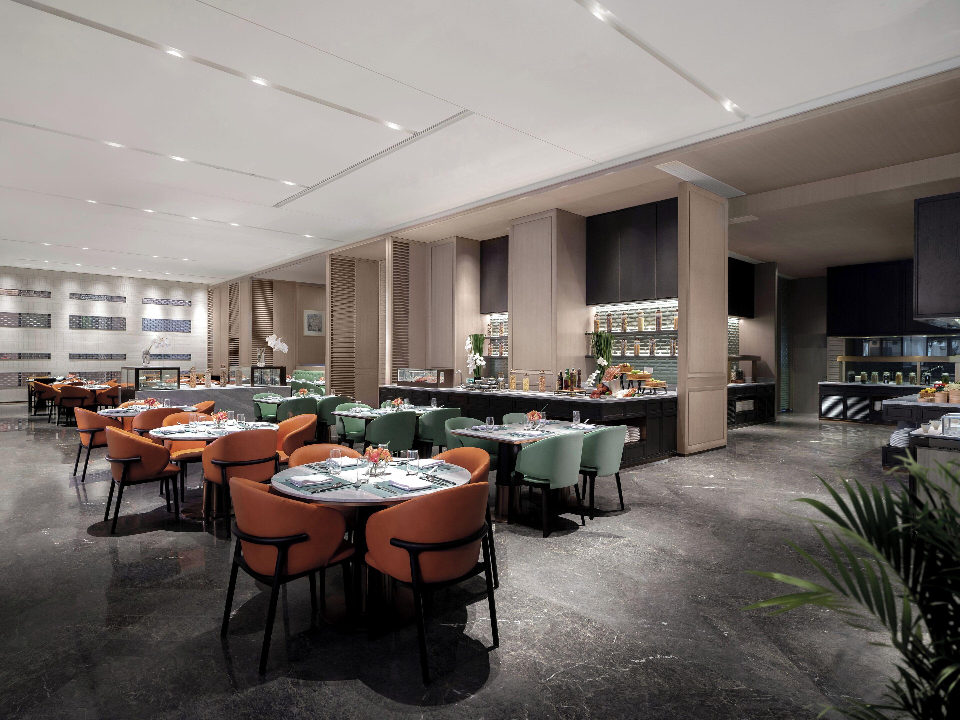 A modern restaurant with round tables and chairs, a bar area, and a kitchen visible in the background.