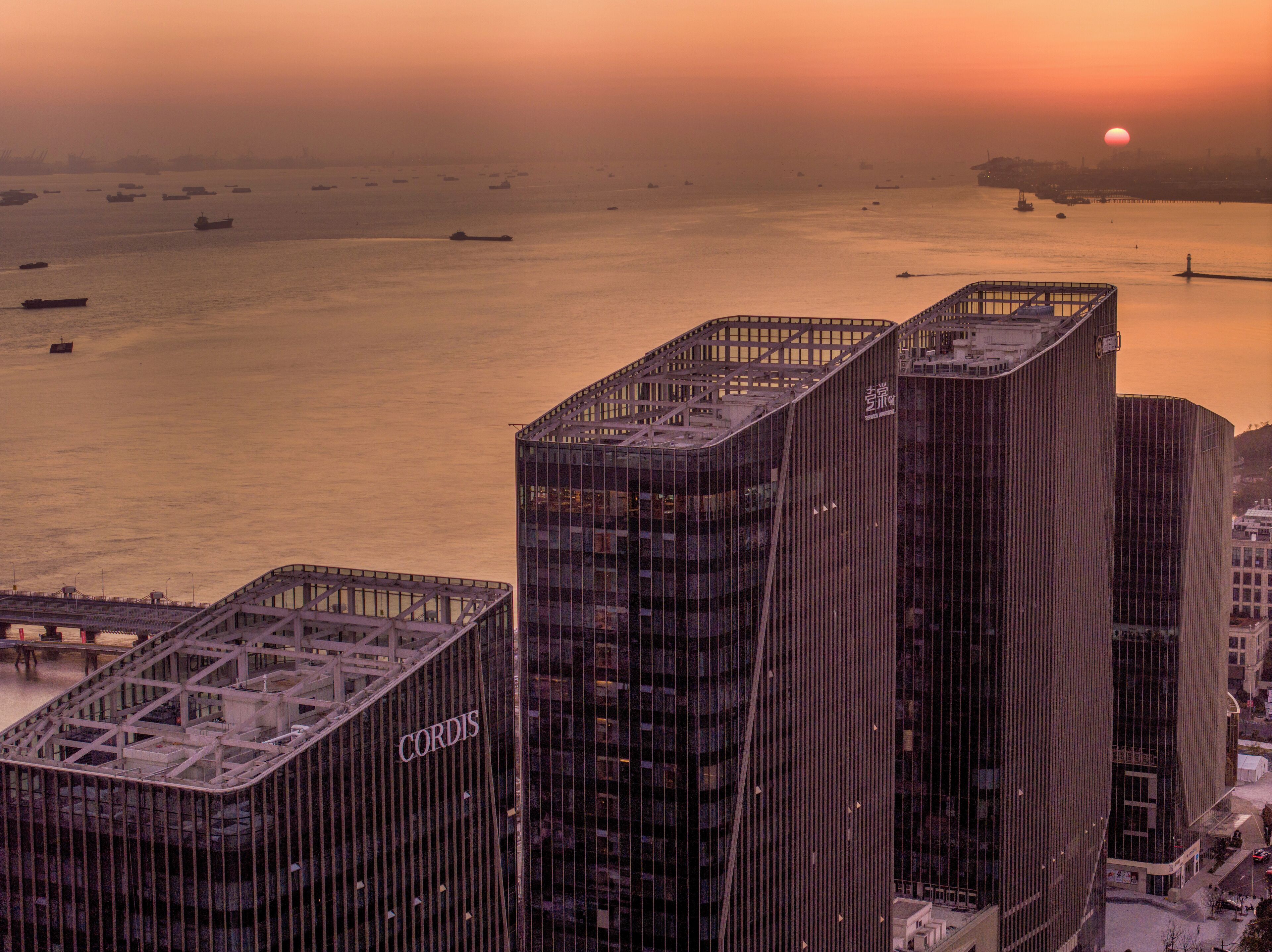 A high-rise building with a prominent 'CORDIS' sign, situated near a waterfront with ships in the background.