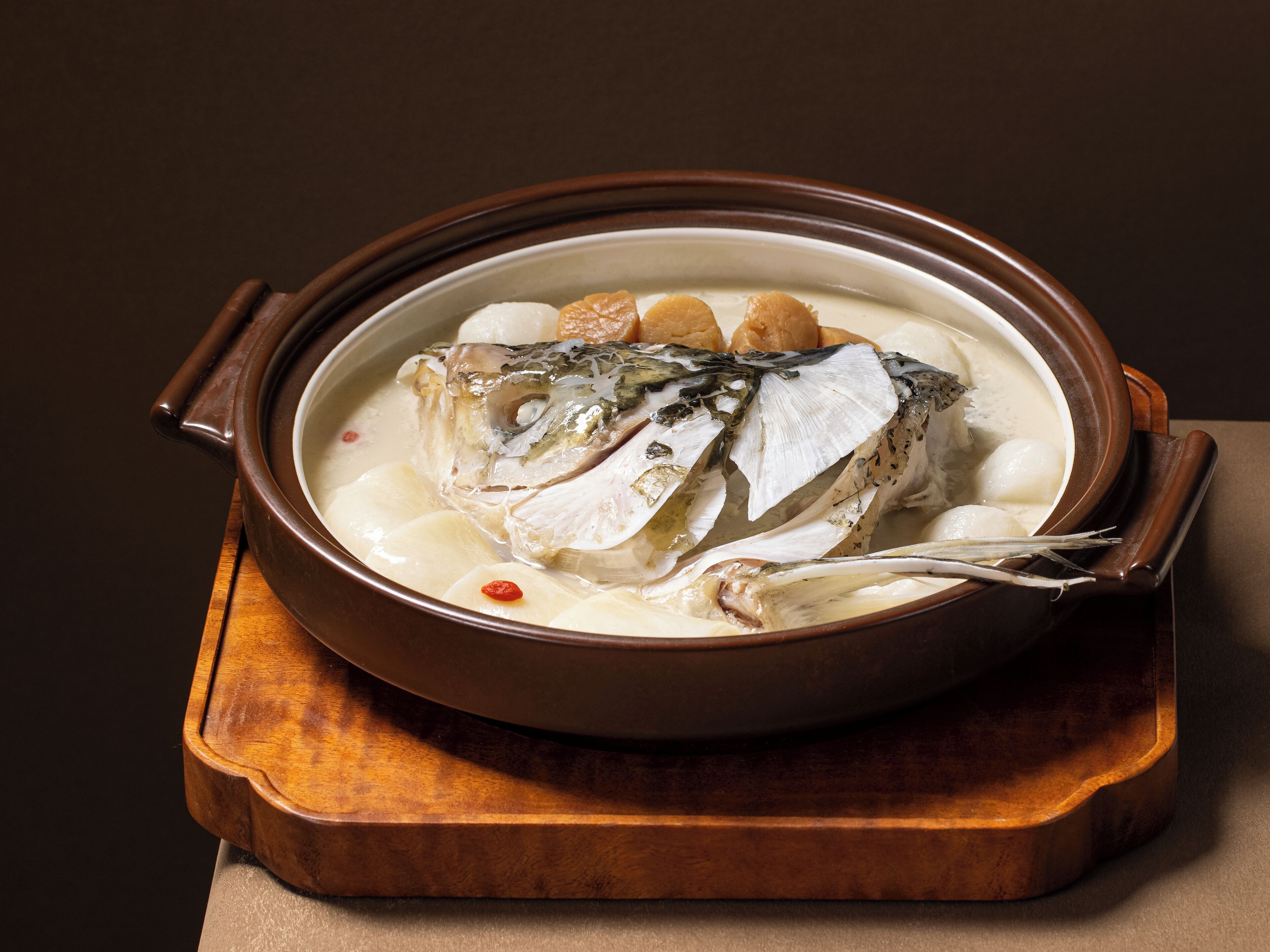 Un tazón de sopa de pescado con tapa, sobre una tabla de madera.