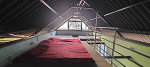 An attic room with a sloped ceiling, a bed with red bedding, and a view through a window. - JRN Island Beach Stay Resort (Honavar)