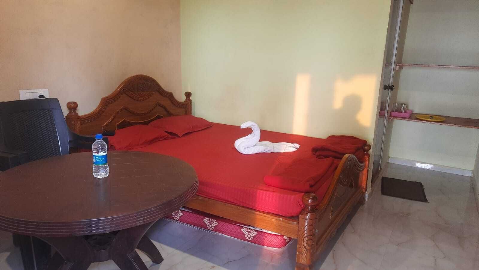 Une chambre d’hôtel avec un lit en bois, une couvre-lit rouge, une serviette en forme de cygne, une bouteille d’eau et une table ronde.