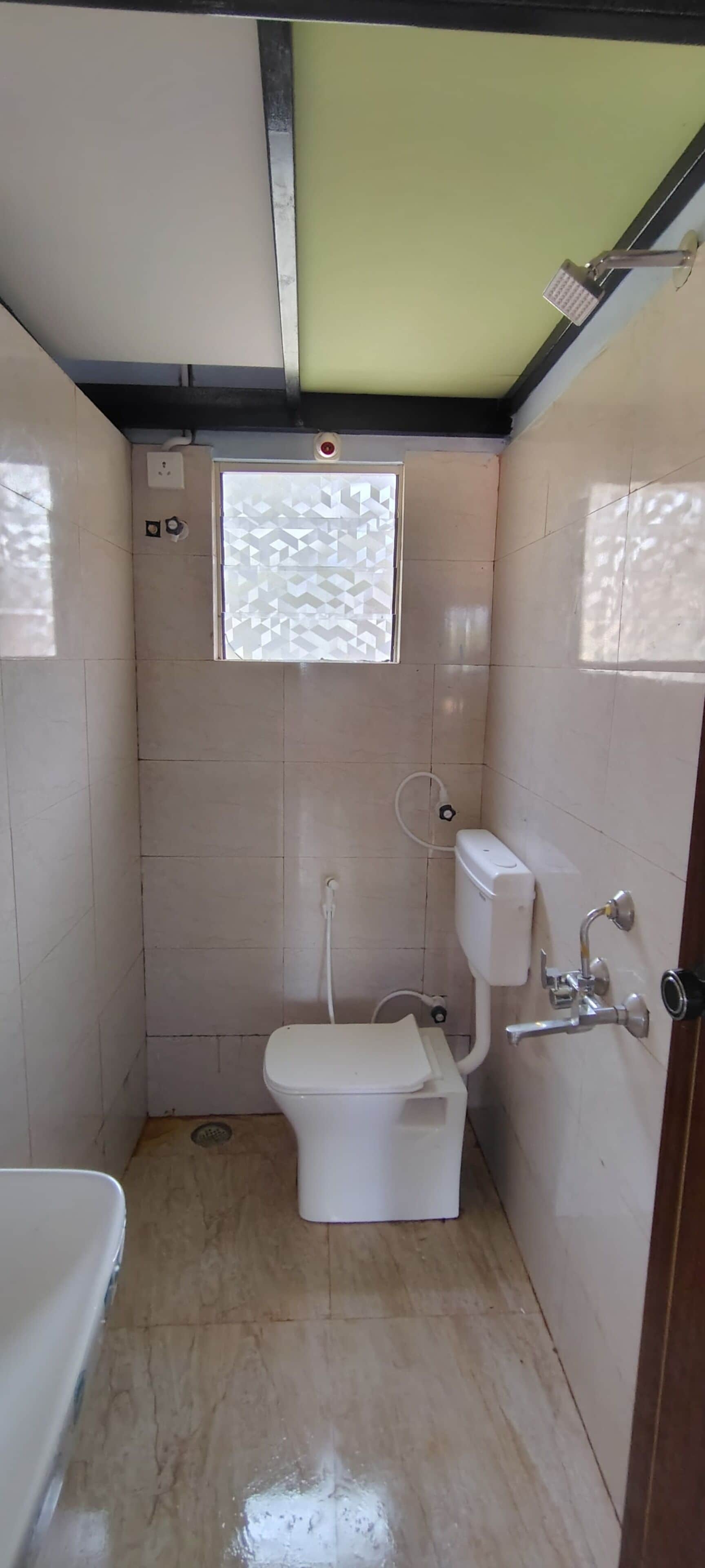 A small, tiled bathroom with a toilet, a shower, and a window with a geometric pattern.