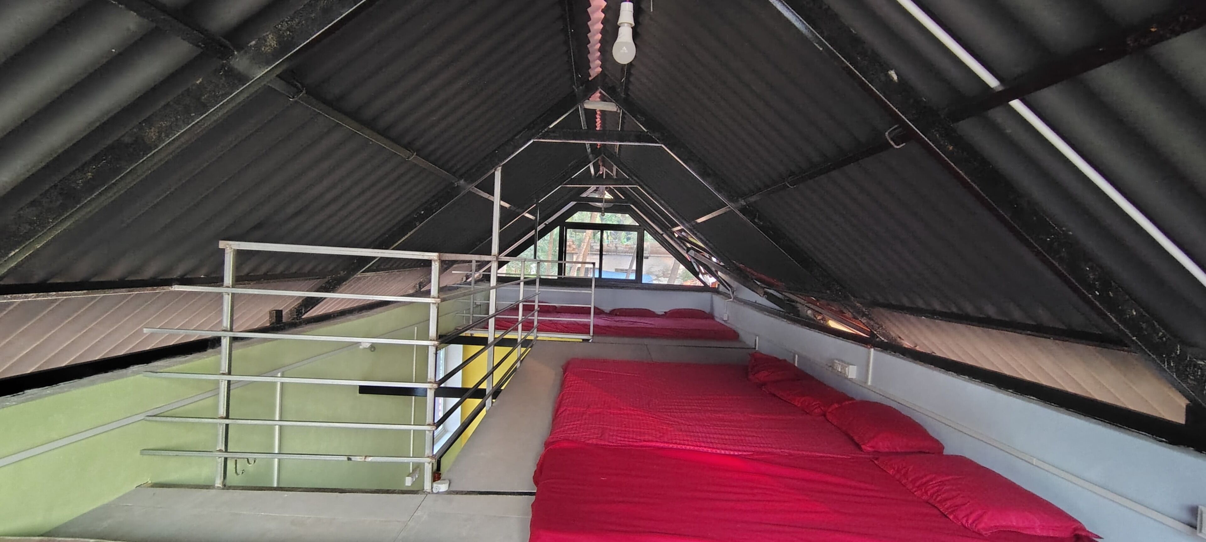 An attic room with a sloped ceiling, a metal ladder, a red bed, and a view through a window.