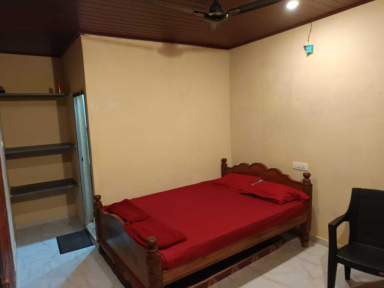 A single bed with a wooden frame and a red bedspread in a room with beige walls and a sloped ceiling.