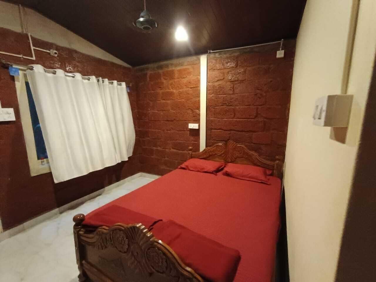 Una camera da letto con un letto in legno, biancheria rossa, un muro in mattoni e una tenda bianca.
