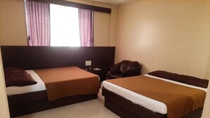 Habitación de hotel con dos camas, una ventana con cortinas, una mesita de noche y un sillón de cuero.