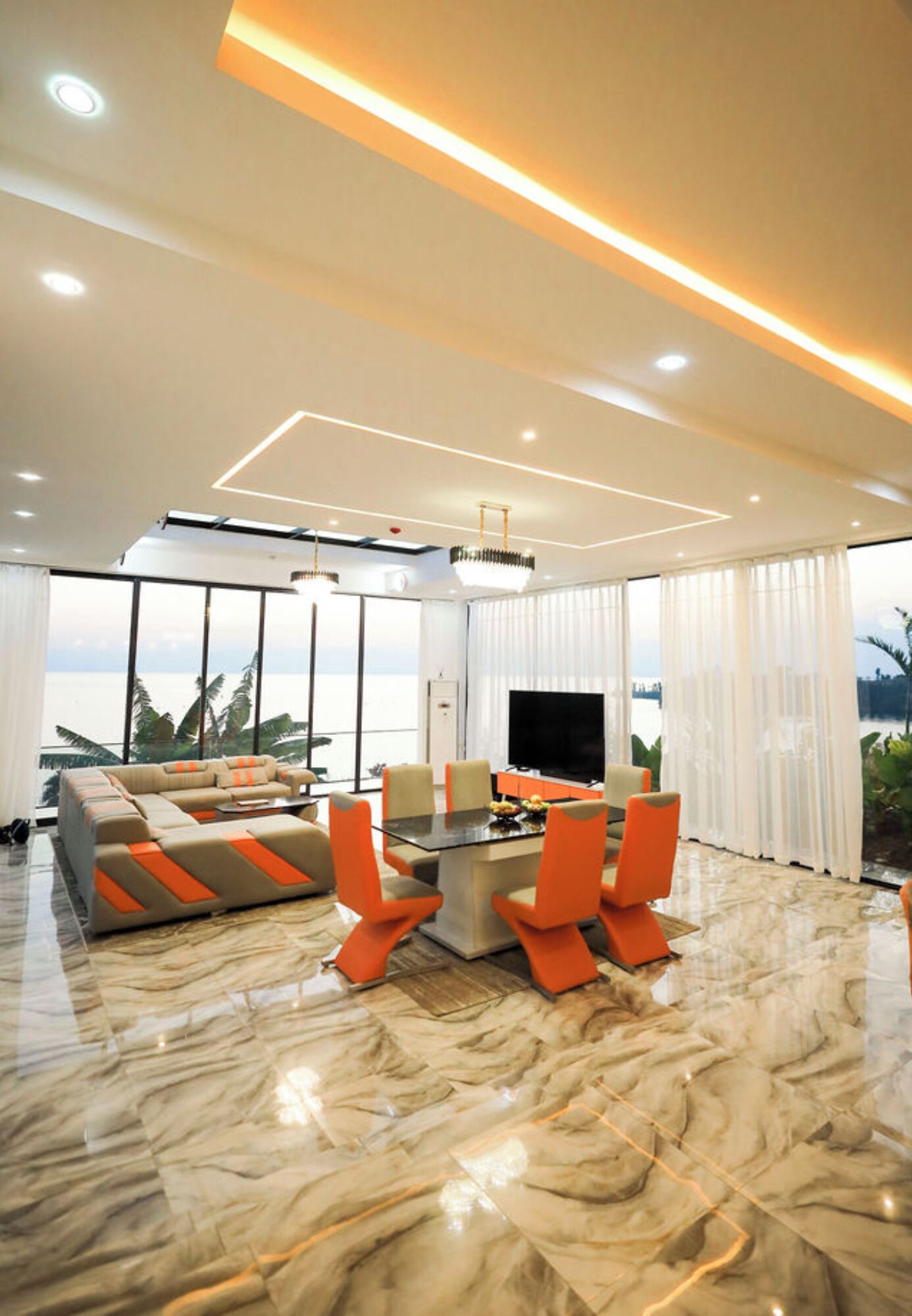 A modern living room with a sofa, orange chairs, a TV, and a large window with a view.
