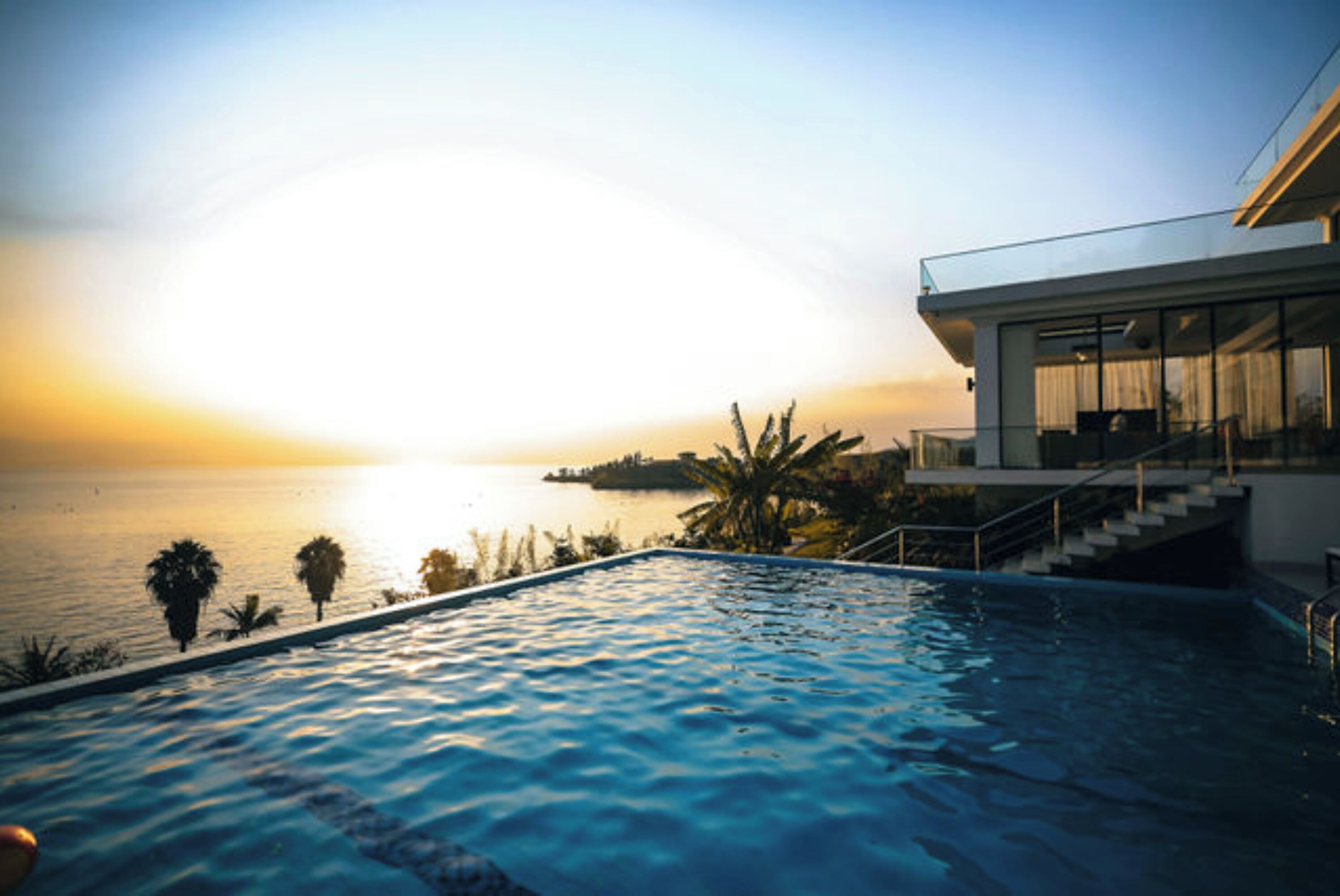 Une piscine à débordement moderne offrant une vue sur l’océan au coucher du soleil.