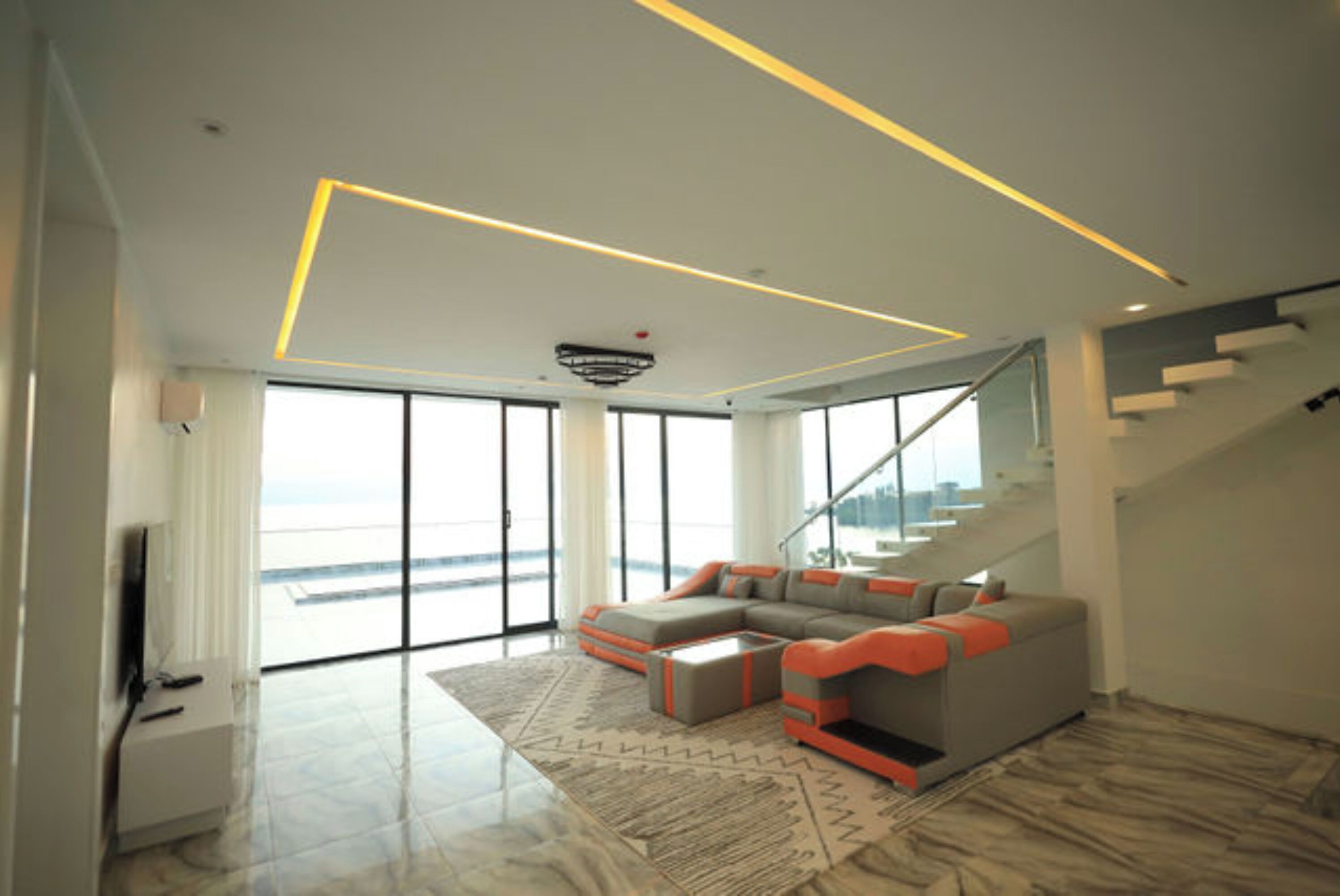 A spacious living room with a large sectional sofa, a flat-screen TV, and a staircase leading to an upper floor.