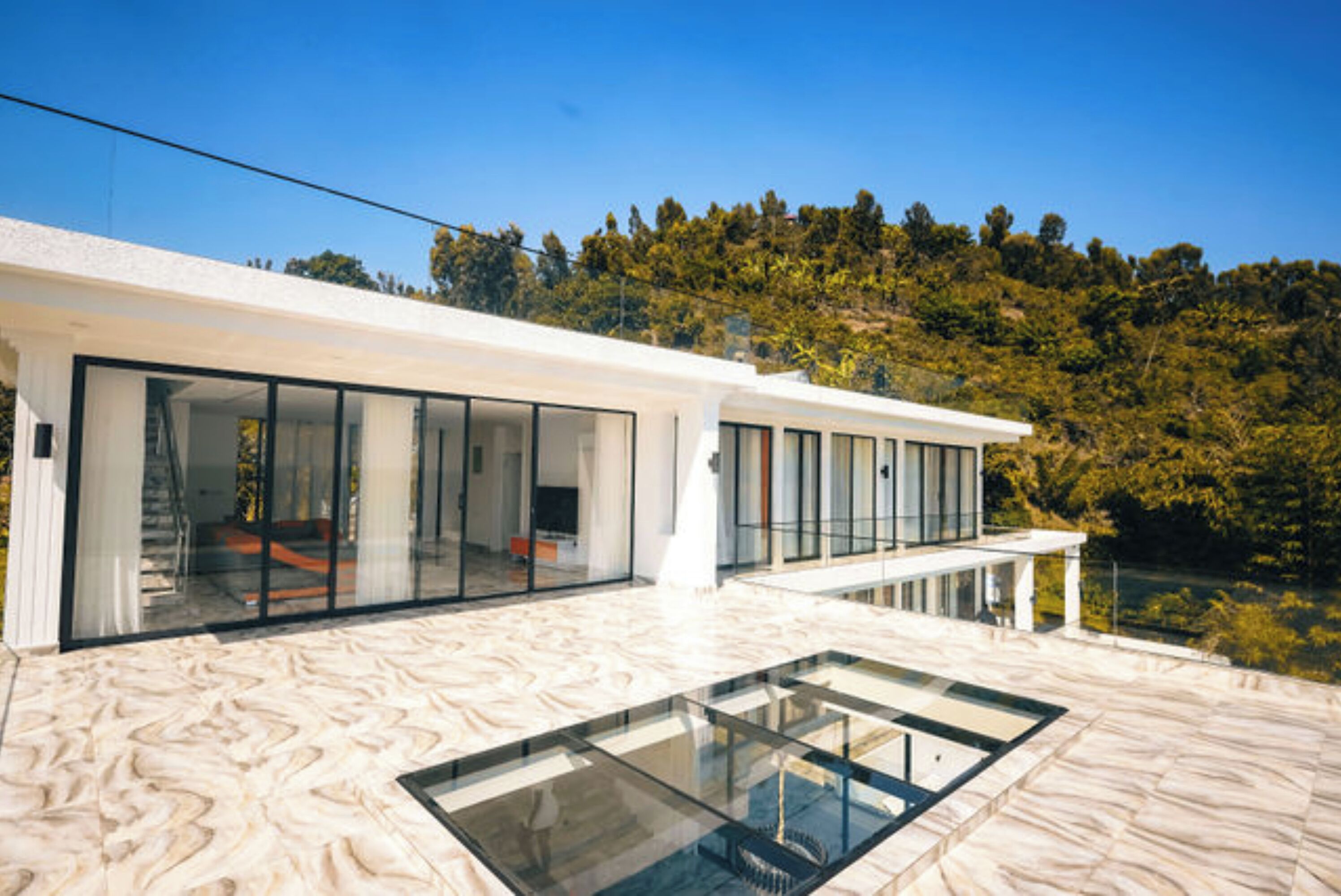 A modern house with large glass windows and a glass floor leading to a lower level.