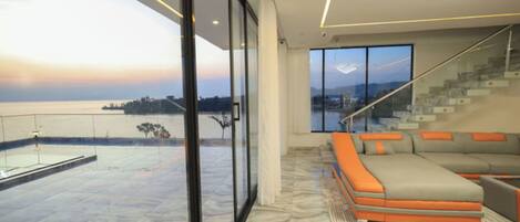 A modern living room with a large window, a glass-enclosed balcony, and a staircase leading to an upper level.