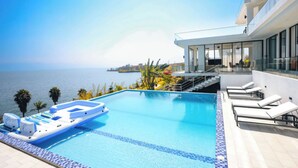 Ein moderner Poolbereich mit freiem Blick auf das Meer, einer schwimmenden Lounge und einem Gebäude mit großen Fenstern.